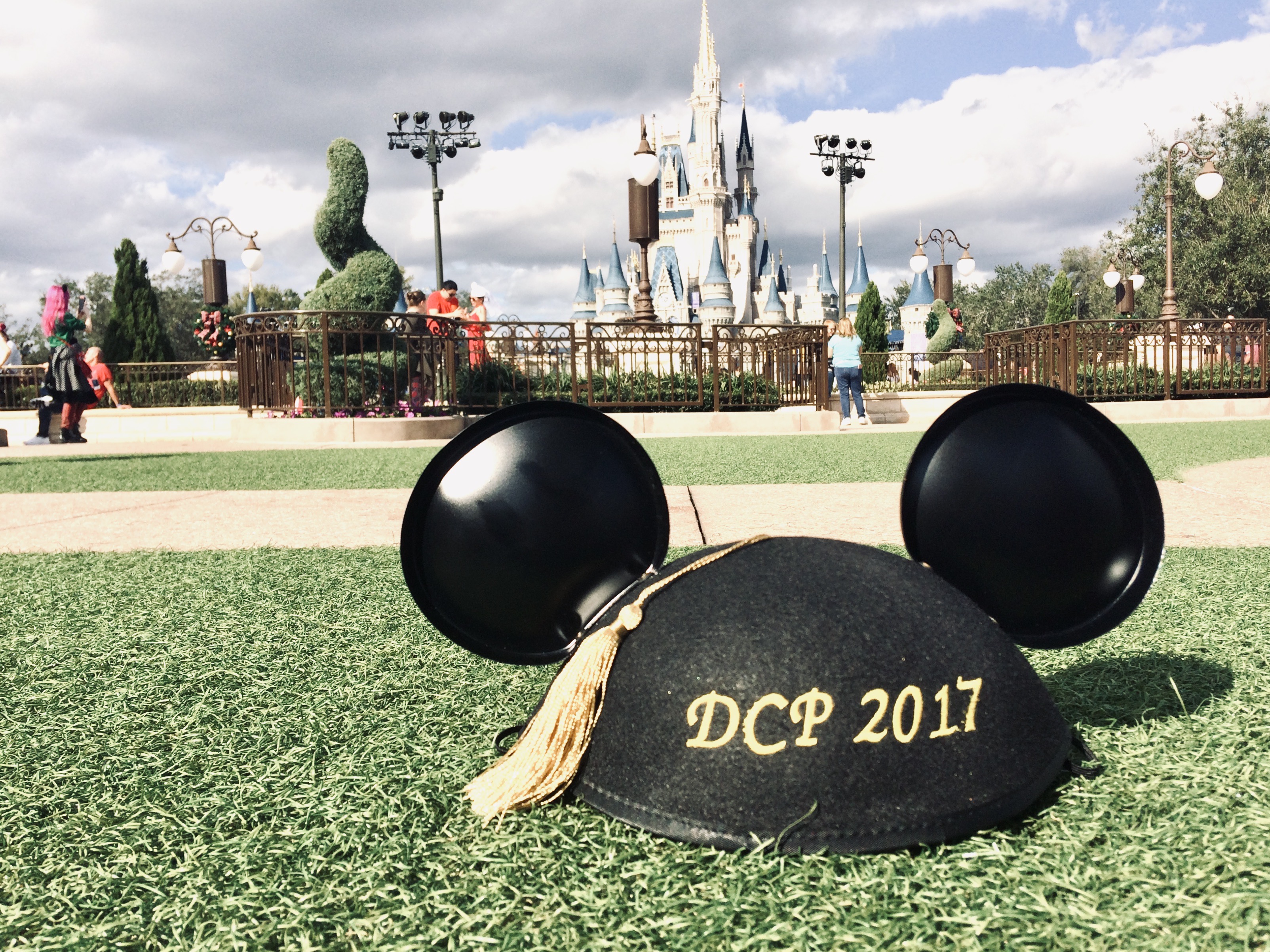 Disney college program graduation ears on hub grass at magic kingdom with Cinderella castle in the background