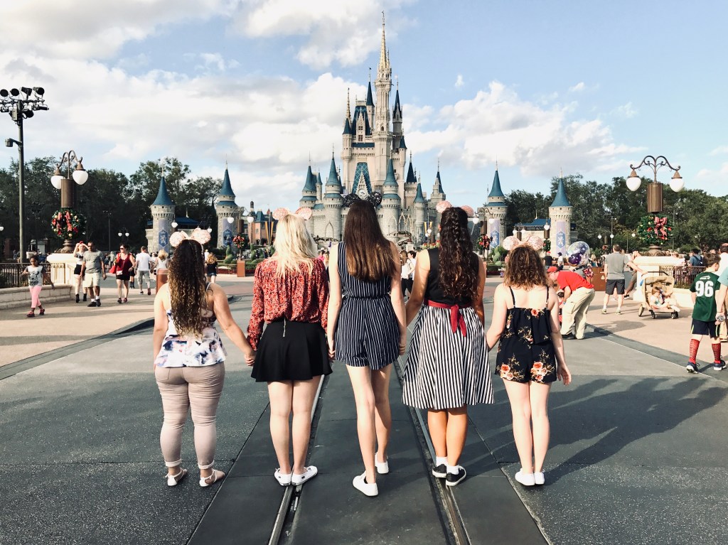 Five Disney college program participants holding hands while standing in front of Cinderella castle at magic kingdom