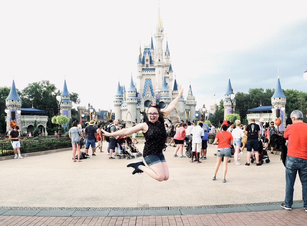 Girl jumping in front of the Walt Disney World castle with mickey mouse ears on.