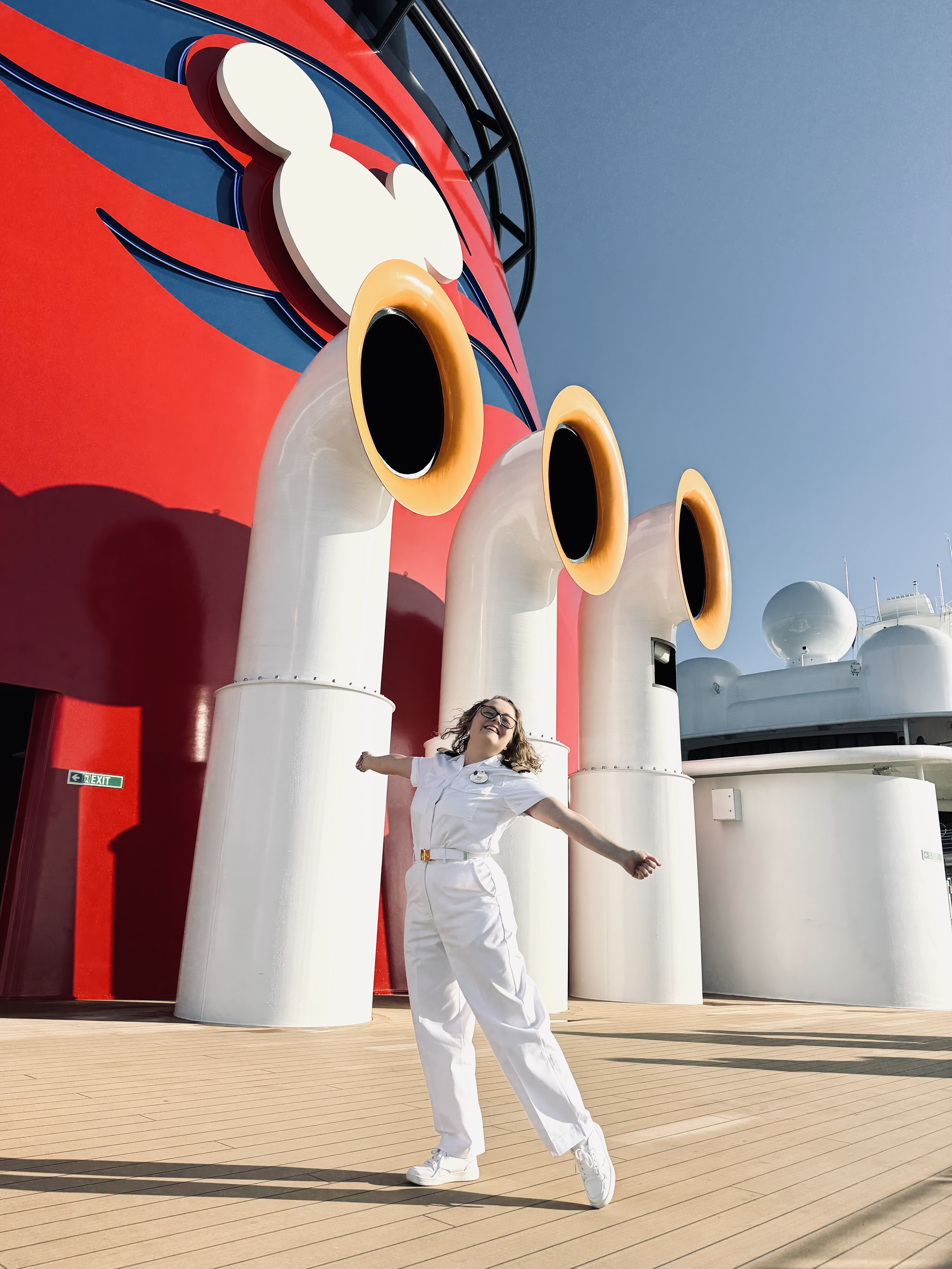 Disney cruise line crew member dressed in officer whites, happy in front of Mickey funnels on a Disney cruise ship