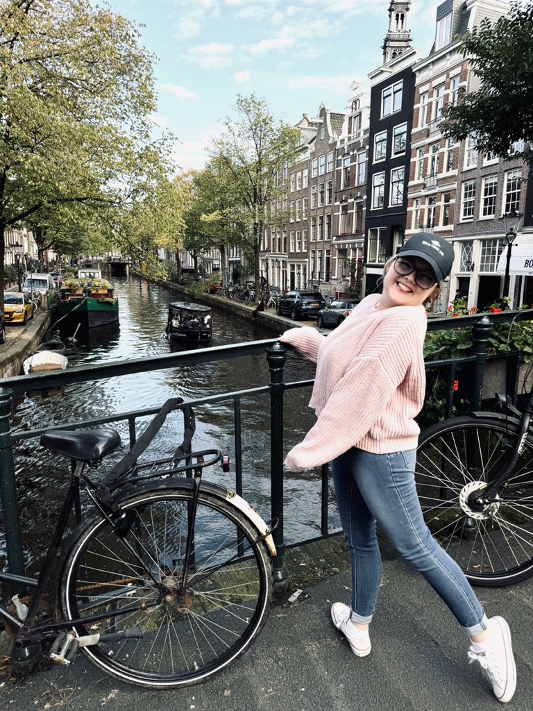 Girl smiling on bridge with colorful houses along a canal with bicycles and green trees in Amsterdam, The Netherlands