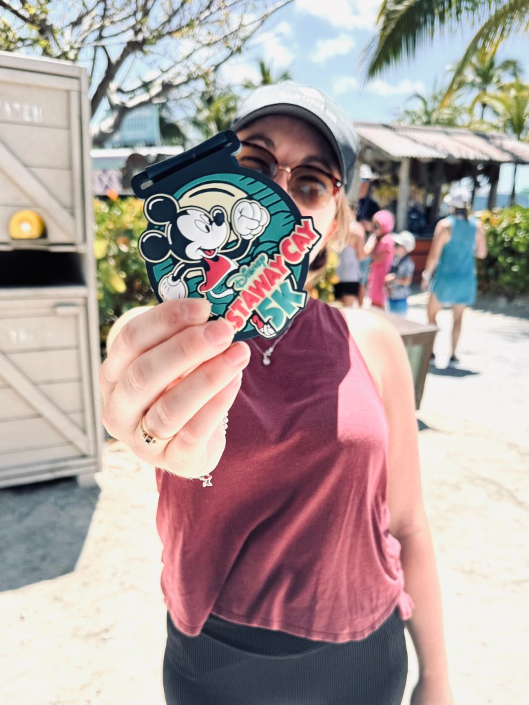 Girl holding a Castaway Cay 5k medal with beach in the background.