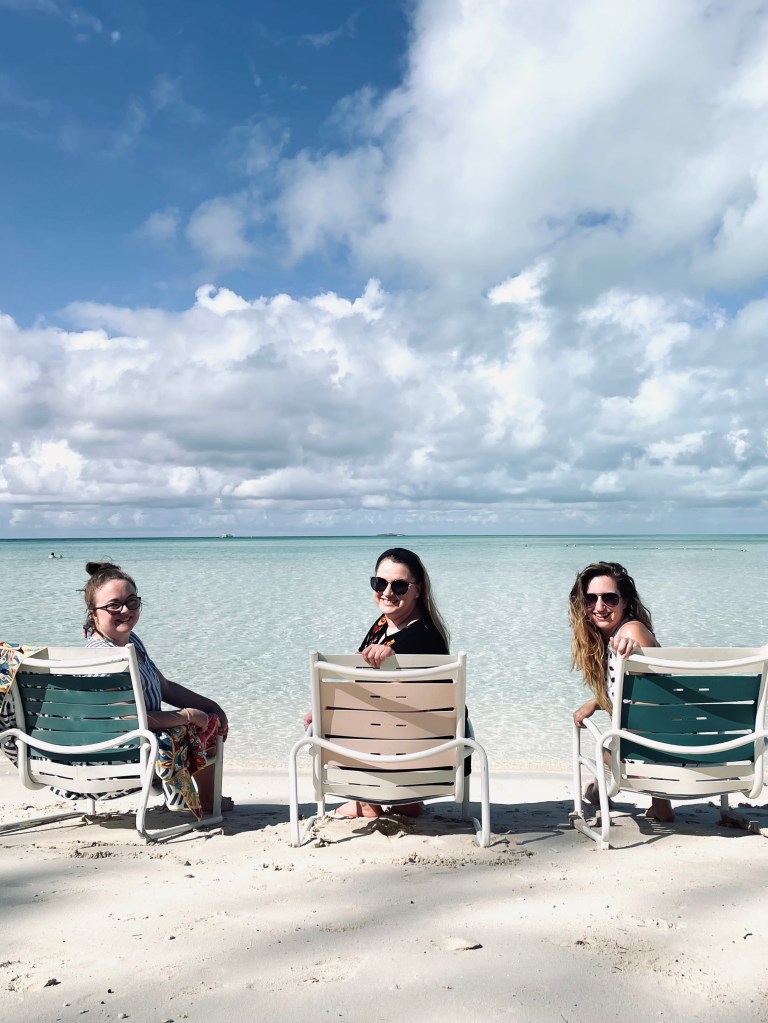Three girls sitting on beach chairs at Castaway Cay, looking back and smiling.
