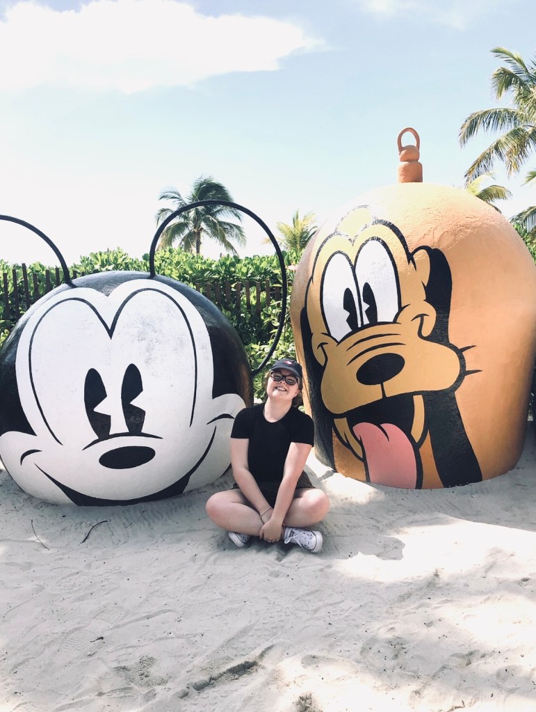 Girl sitting next to Mickey and Pluto themed bouys at Disney's Private Island Castaway Cay