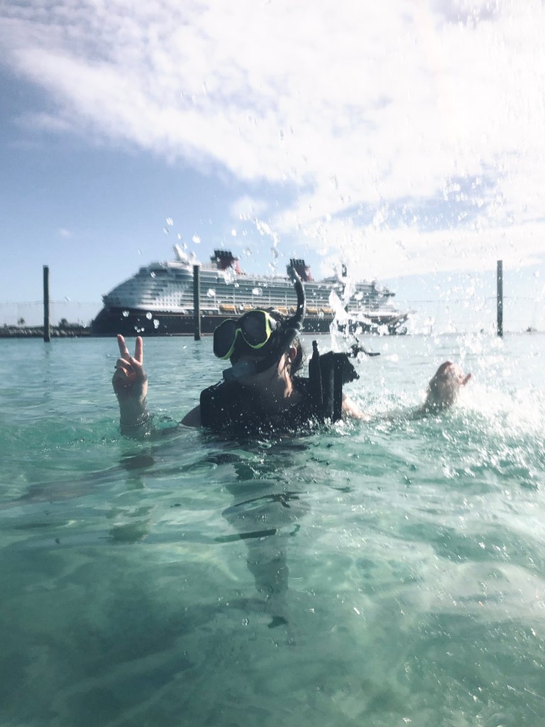 Girl swimming in the ocean with snorkel mask, with water splashing and a Disney Cruise Ship in the background.