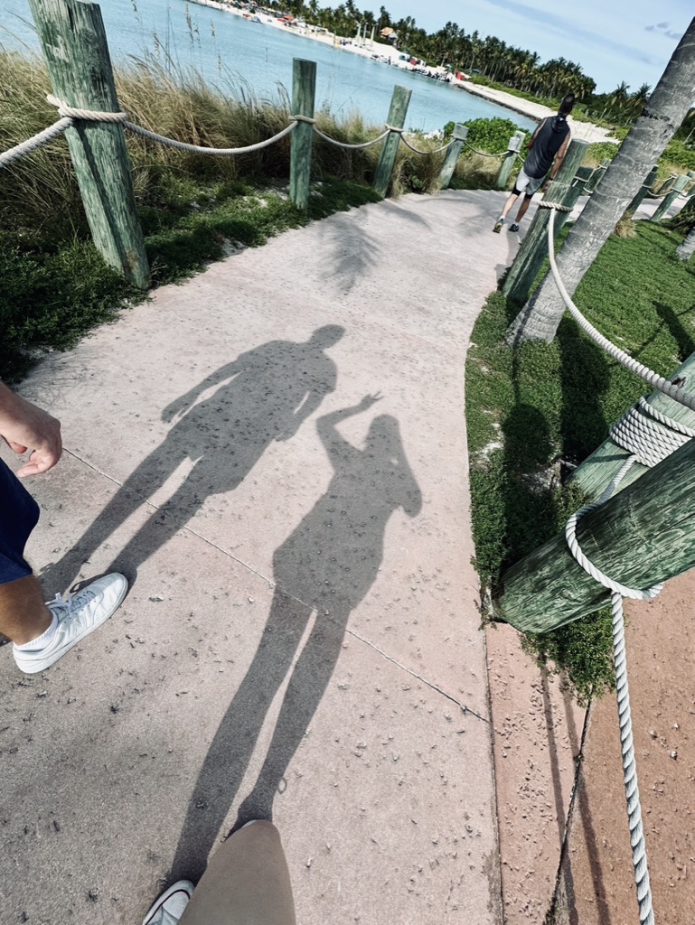 Two people walking on footpath with shadows towards castaway cay.