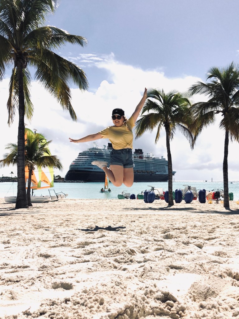 Girl jumping on beach with palm trees and disney cruise ship in the background at Castaway Cay, Bahamas