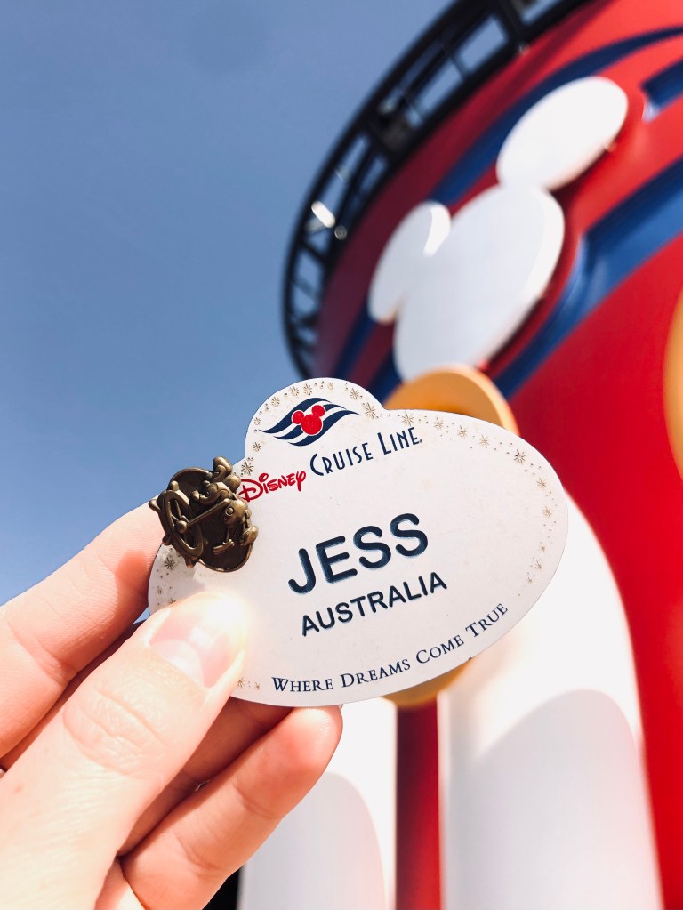 Disney Cruise Line Crew Member nametag with 1 year pin. Red Mickey funnels in background.