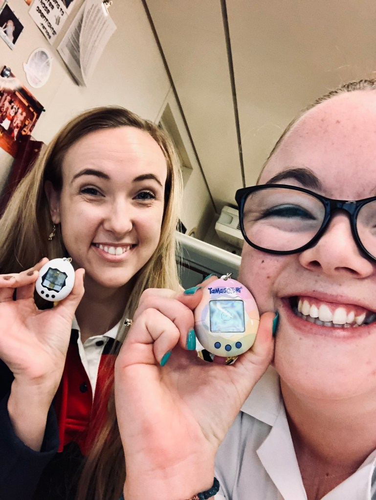 Two girls taking a selfie with tamagotchis in office.