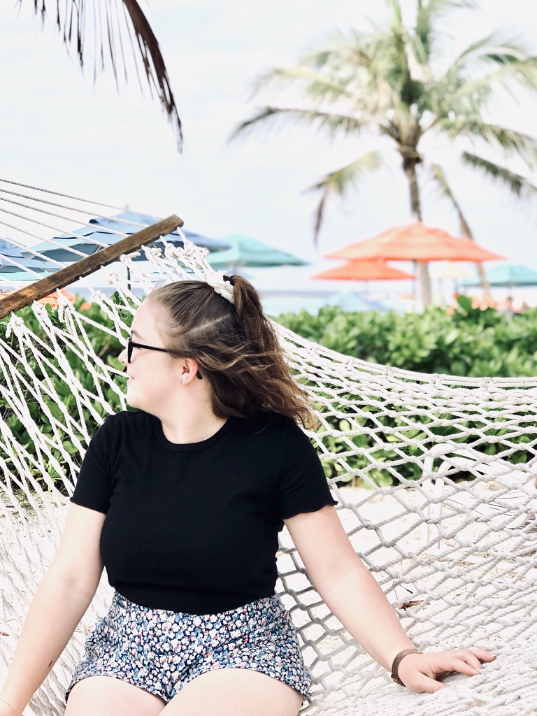 Girl sitting on hammock in Castaway Cay with umbrellas and palm trees in the background