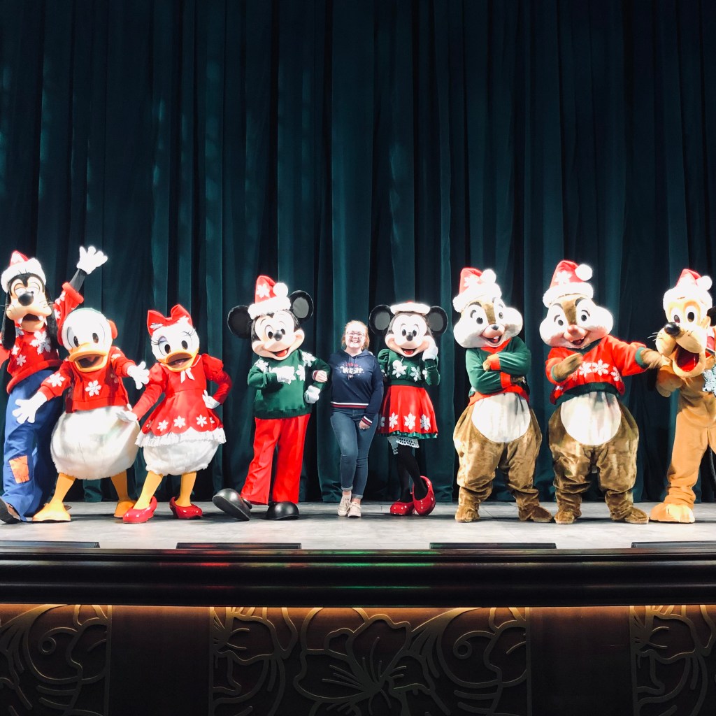 Girl with all Mickey and friends characters dressed in Christmas outfits on a stage on a disney cruise ship