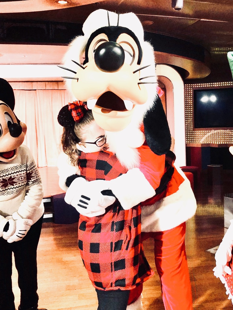GIrl in Christmas outfit hugging Santa Goofy on a disney cruise ship