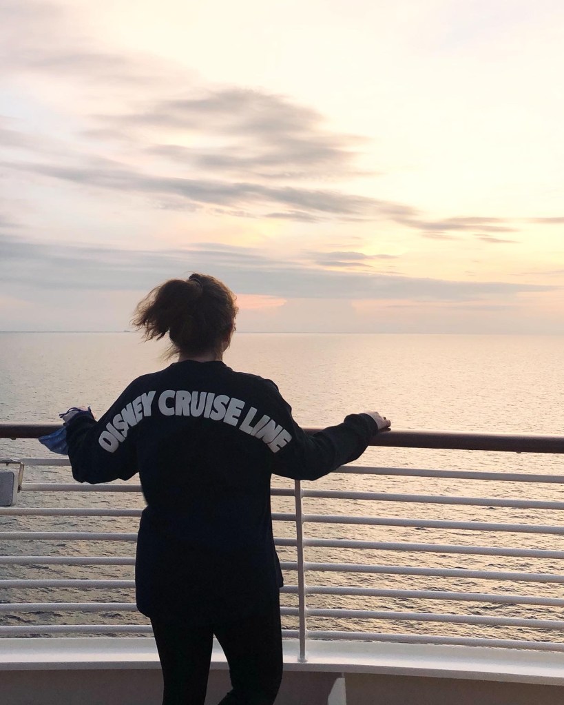 Girl wearing Disney Cruise Line spirit jersey looking out to ocean sunset on a Disney Cruise Ship.