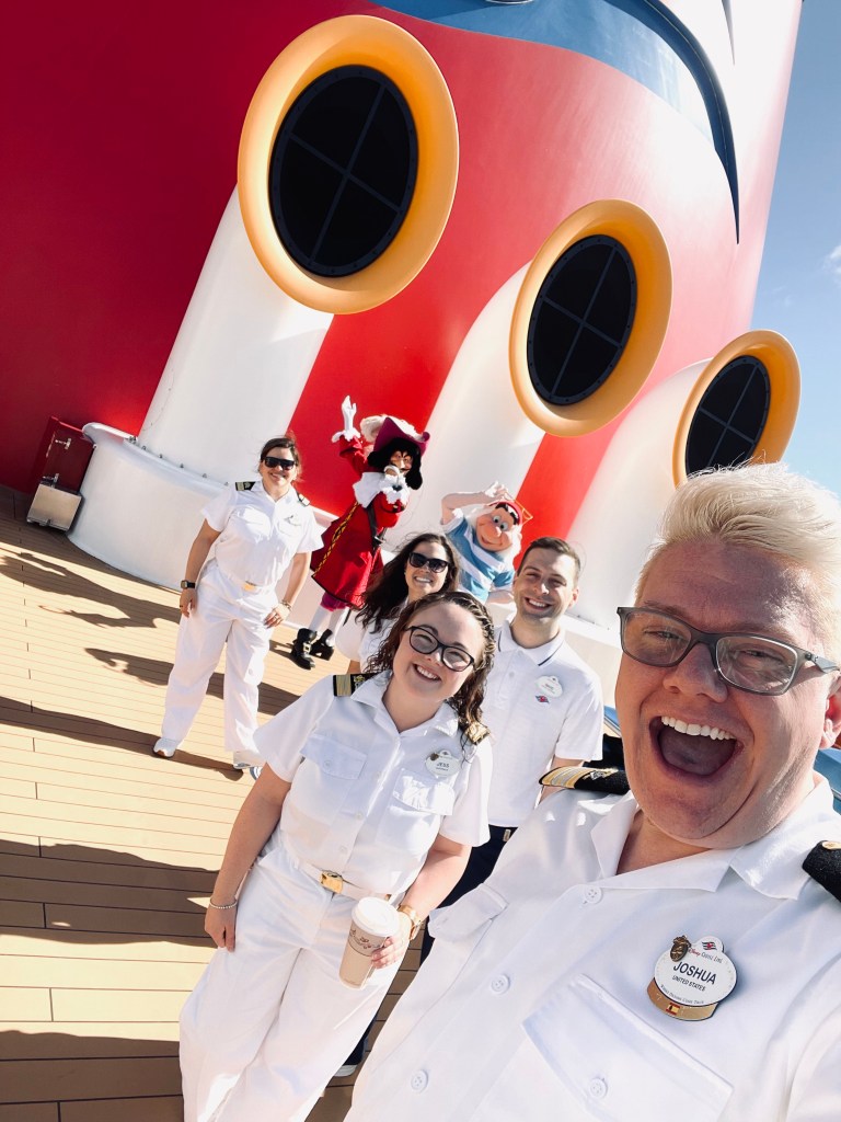 Group of Disney Cruise Line officers taking a selfie with Captain Hook and Smee with mickey funnels in background.
