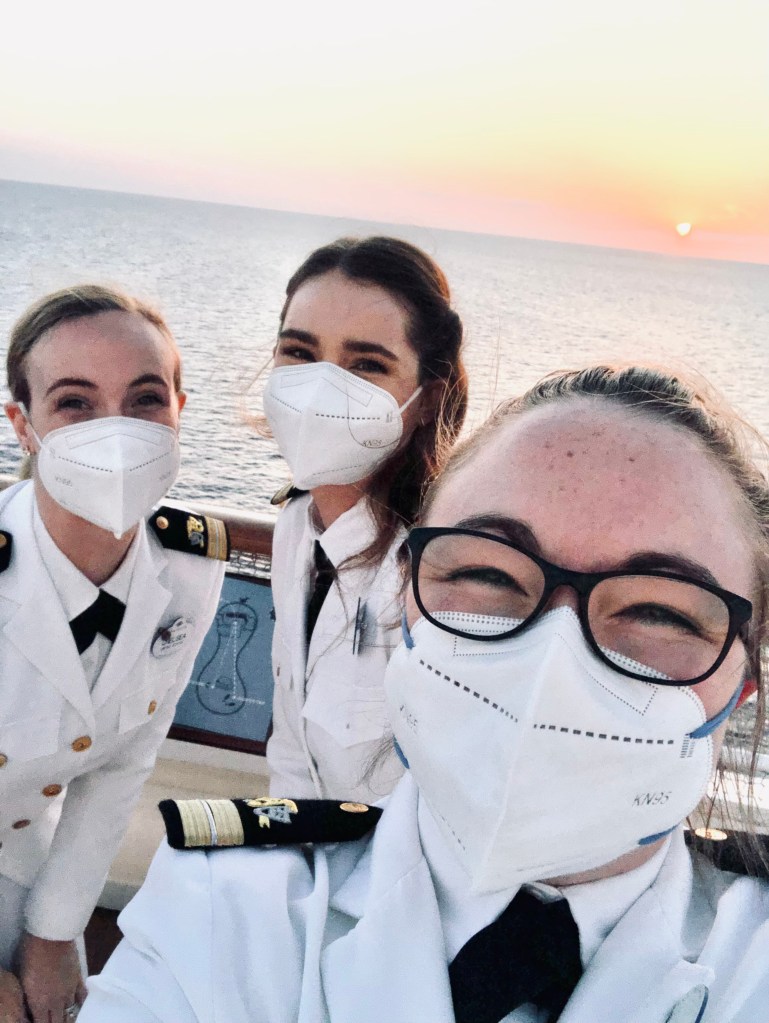 Disney Cruise Line officers wearing face masks taking a selfie with an ocean sunset