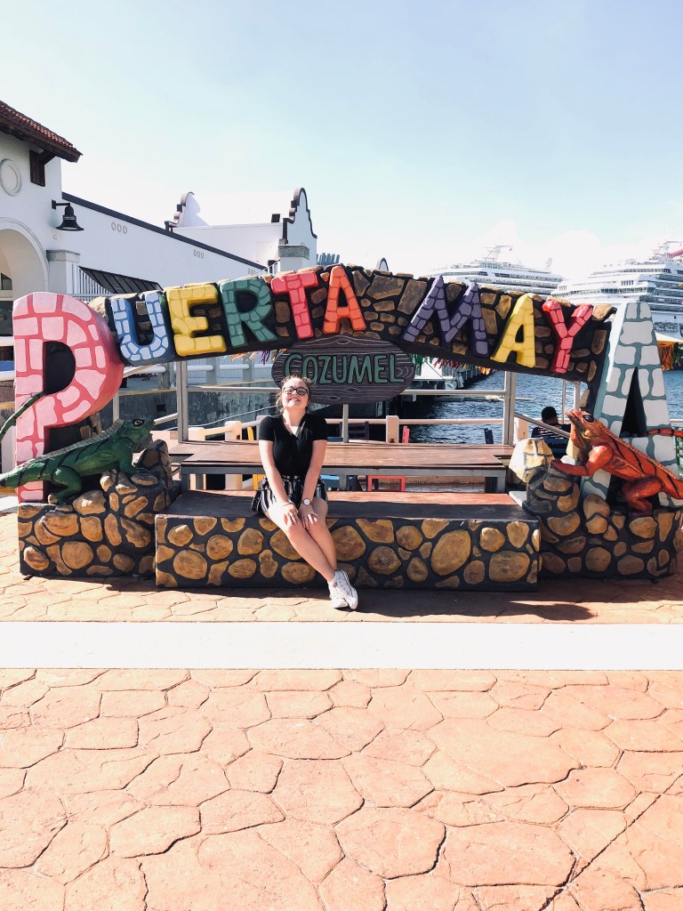 Girl sitting with Puerta Maya port sign in Cozumel, Mexico