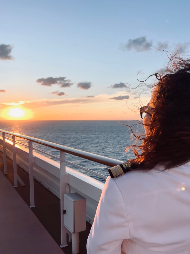 Disney Cruise Ship officer looking out at sunset on the ocean from cruise ship deck.