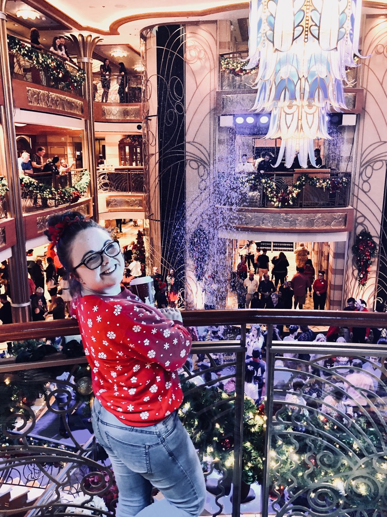 Girl in christmas sweater smiling over balcony on Disney Dream cruise ship with snow in the atrium