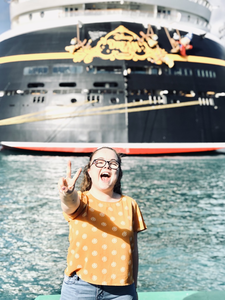 Girl smiling with peace sign in front of Disney Dream cruise ship
