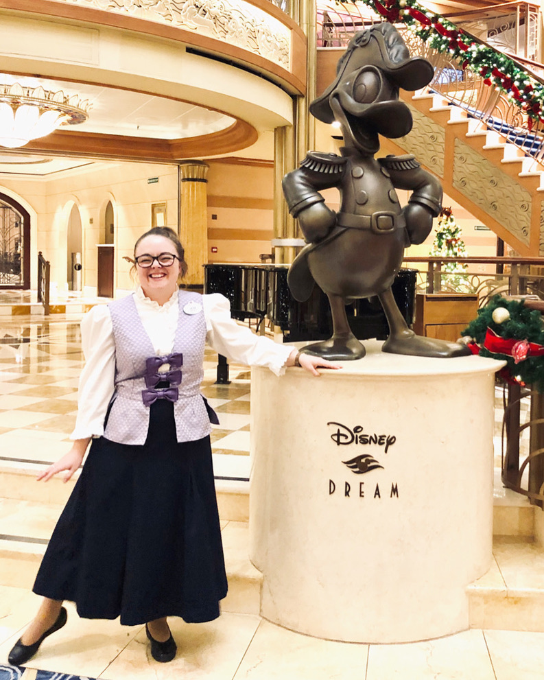 Bibbidi Bobbidi Boutique fairy godmother posing next to Disney Dream cruise ship statue of Admiral Donald