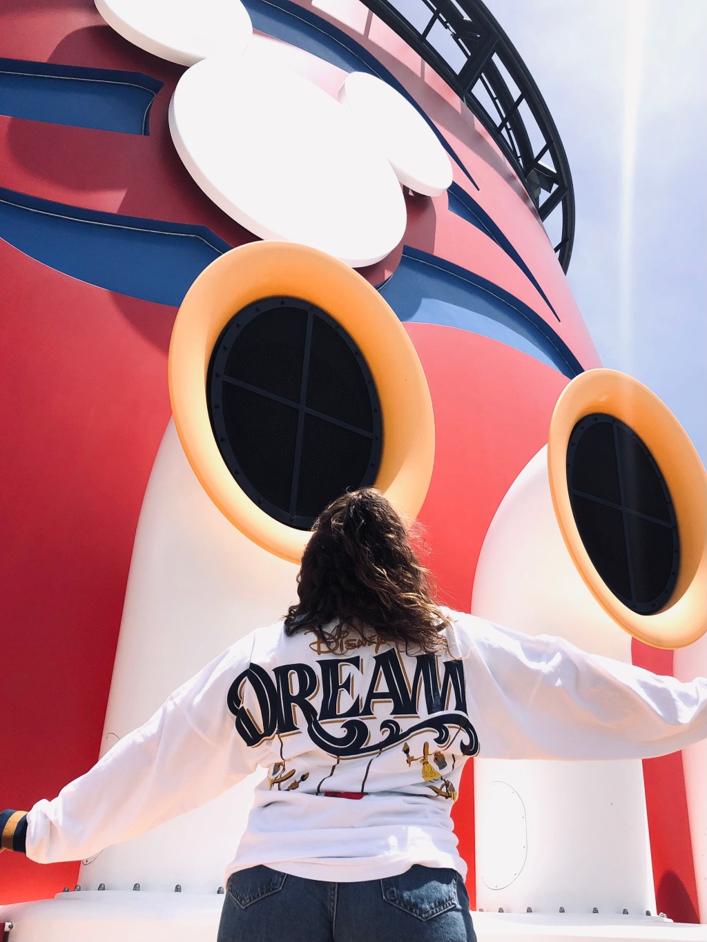 Girl wearing Disney Dream spirit jersey posing in front of Disney Cruise Ship mickey funnels