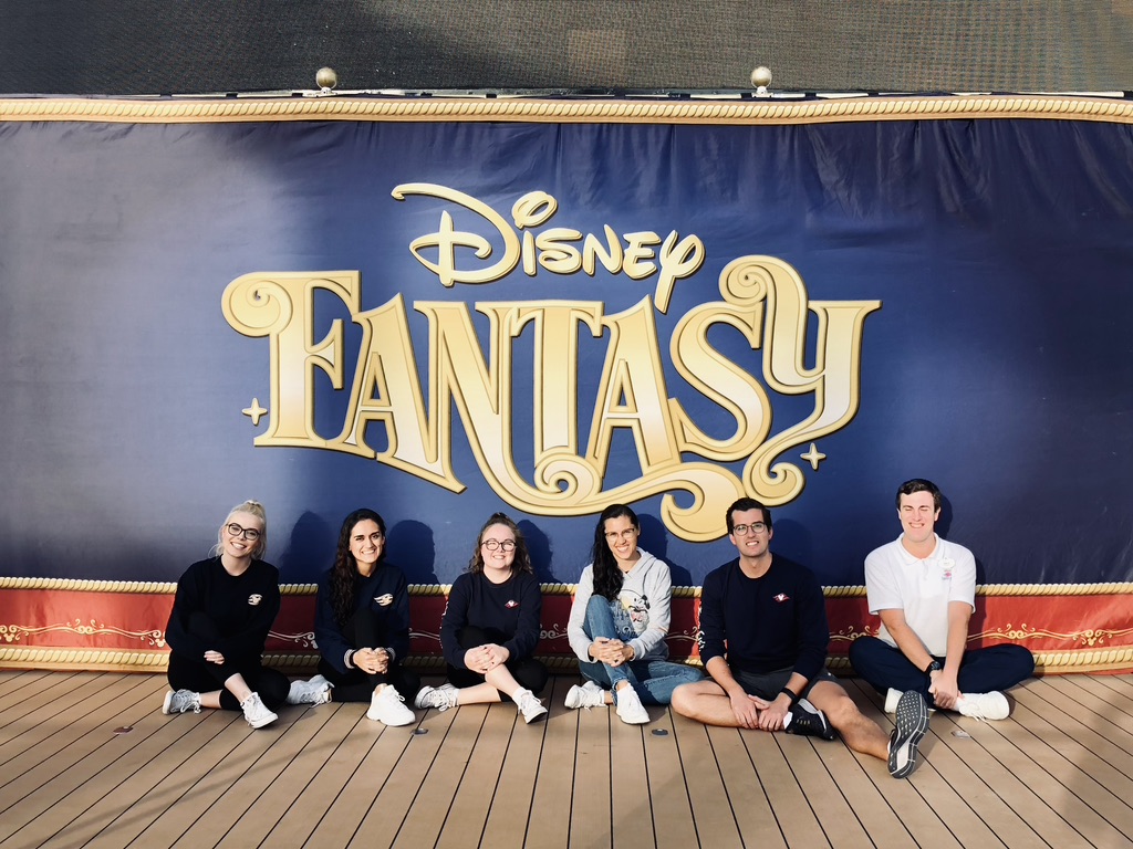 Group of friends in front of Disney Fantasy logo backdrop