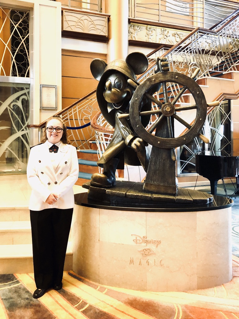 Disney cast member smiling next to Disney Magic cruise ship statue of Mickey Mouse