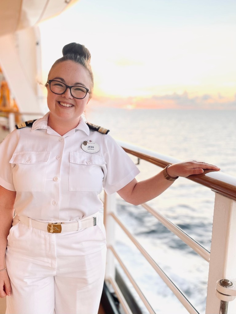 Disney Cruise Line officer smiling on deck in officer whites with ocean sunset in the background.