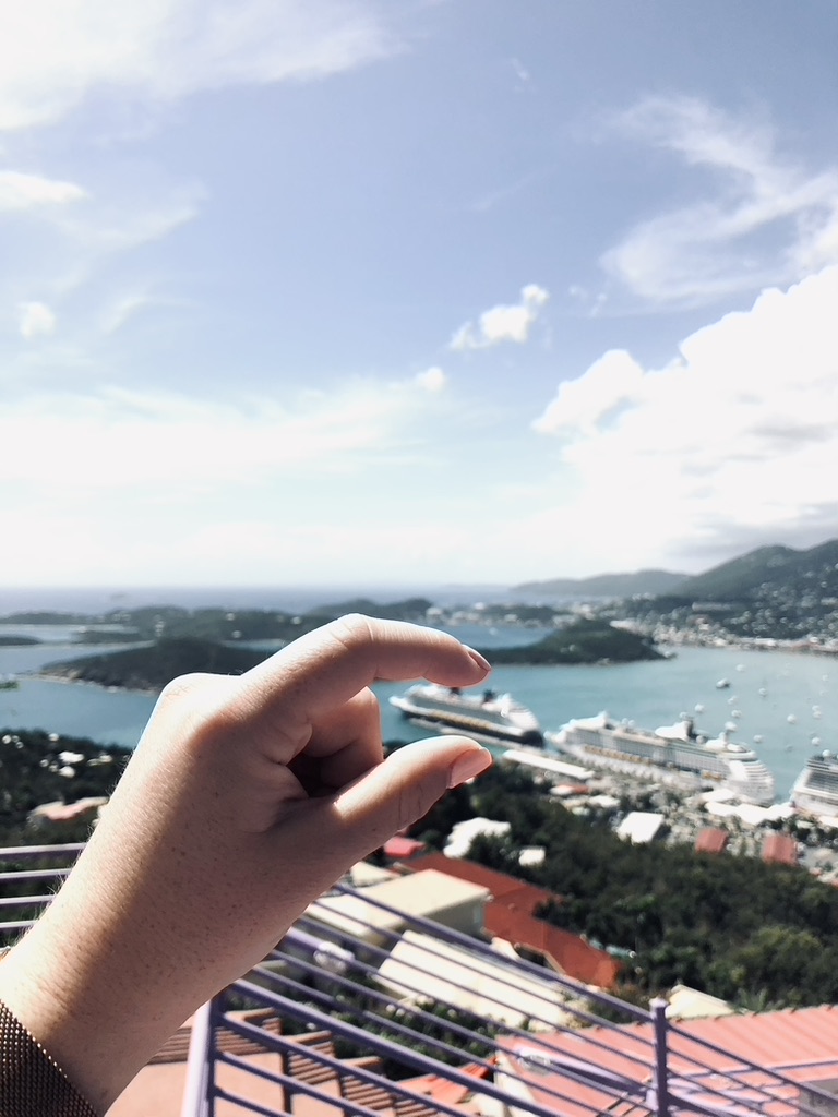 Girl pretending to hold cruise ship with view of St Thomas from Paradise Point observation deck. Ocean, islands and ship in the distance.
