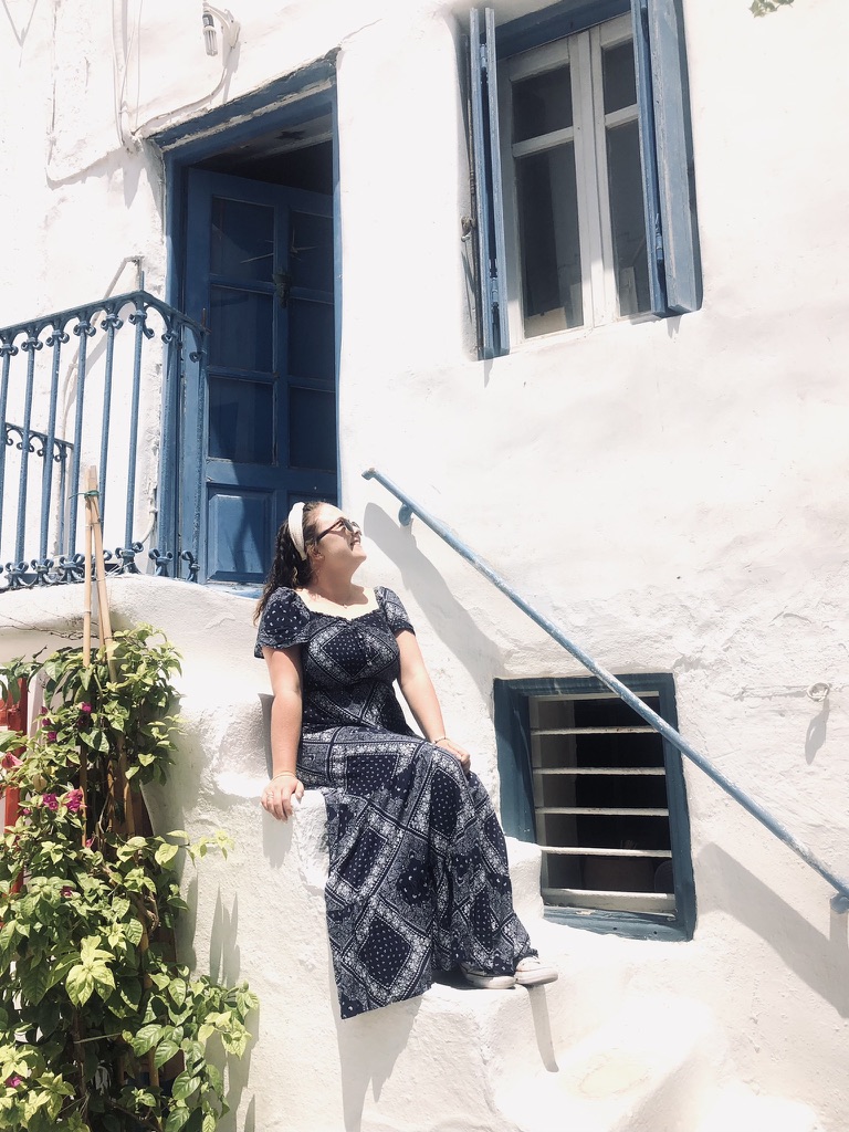 Girl sitting on white steps with blue door at Mykonos, Greece