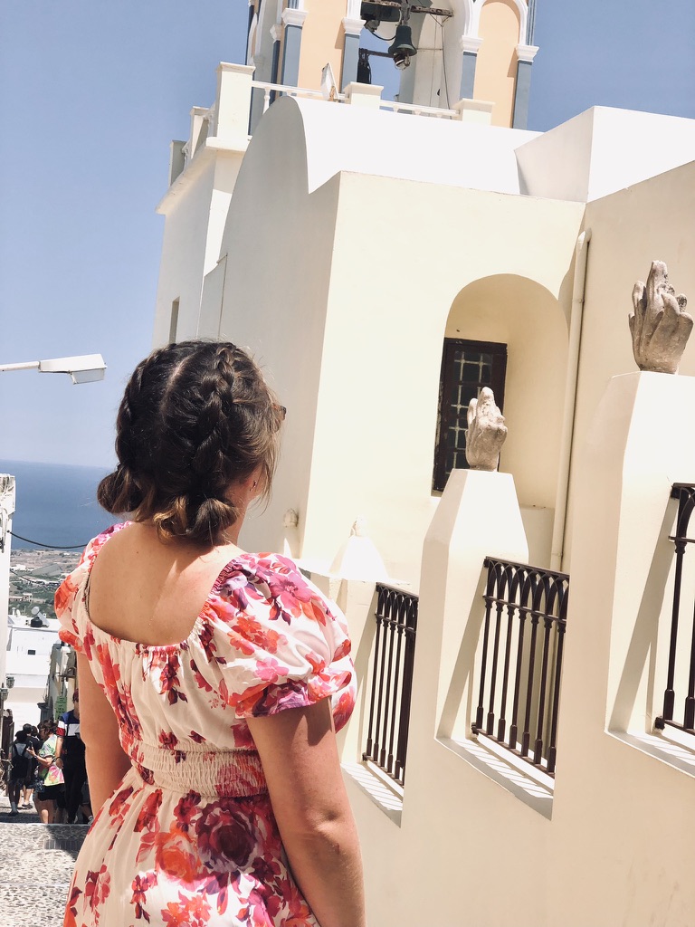 Girl in summer dress looking up at clock tower in Santorini, Greece