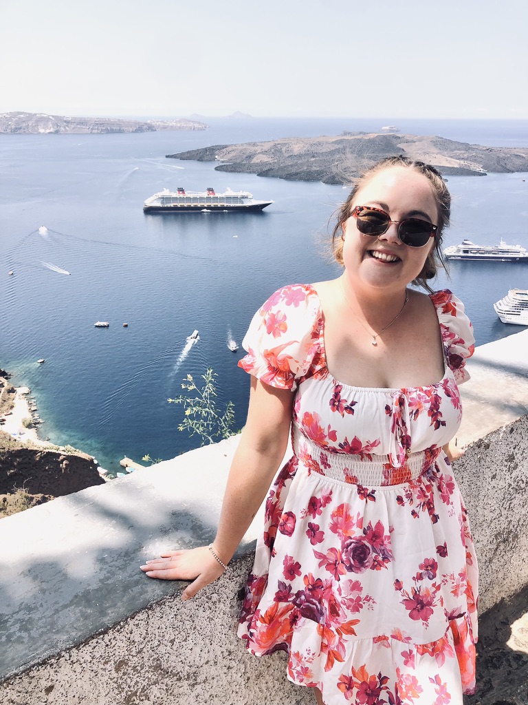 Girl in summer dress smiling with view of ship and greek islands in background from Santorini, Greece