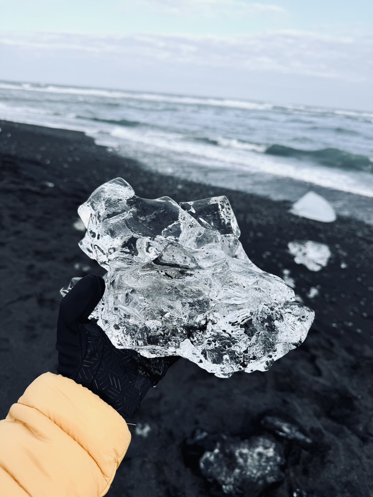 Hand holding a piece of ice washed up on black sand beach at Diamond Beach, Iceland