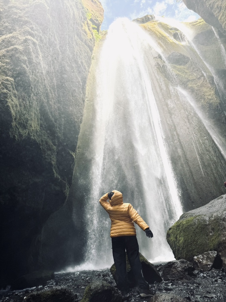 Girl in yellow coat in cave at the base of Gljúfrabúi waterfall, Iceland