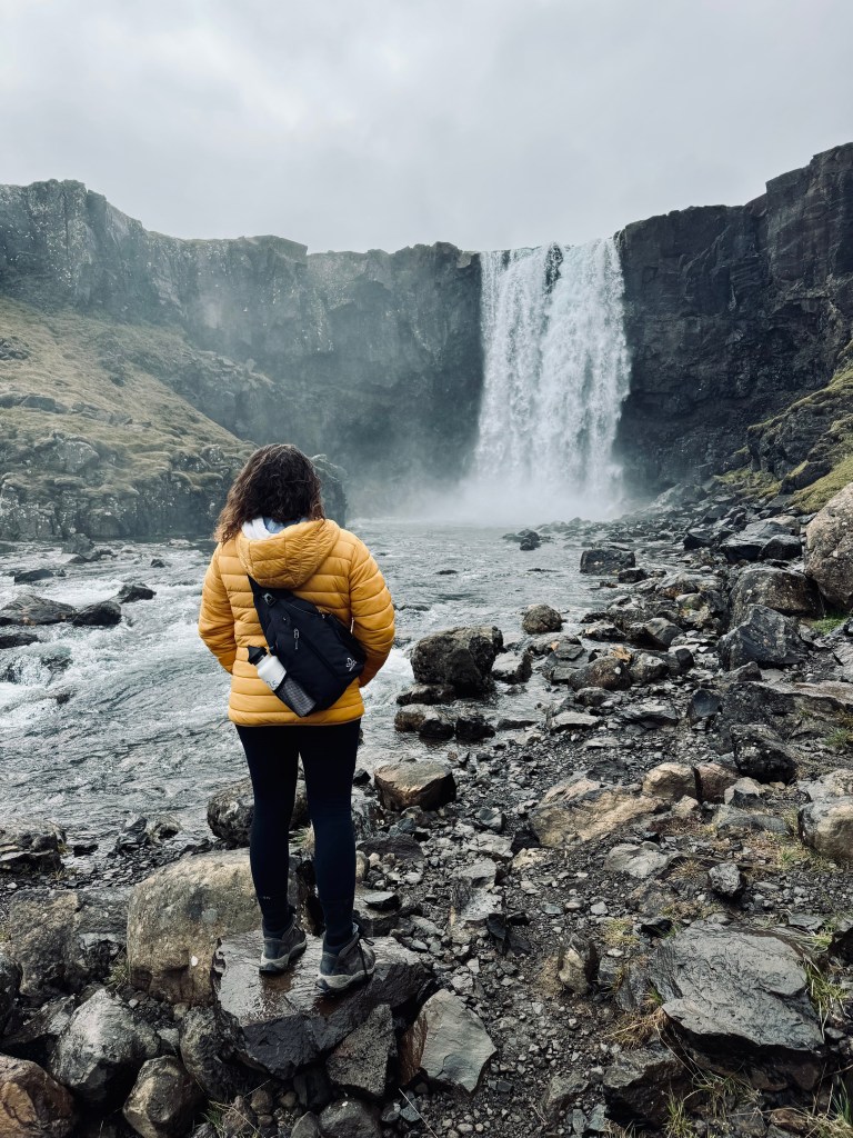 Girl in yellow coat looking at Gufufoss waterfall from rocks in Iceland