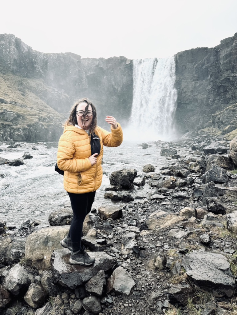 Girl in yellow coat laughing in the wind in front of Gufufoss Waterfall in Iceland