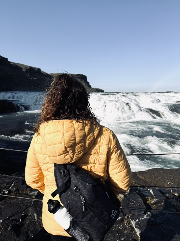 Girl in yellow coat looking out at Gullfoss Waterfall, Iceland