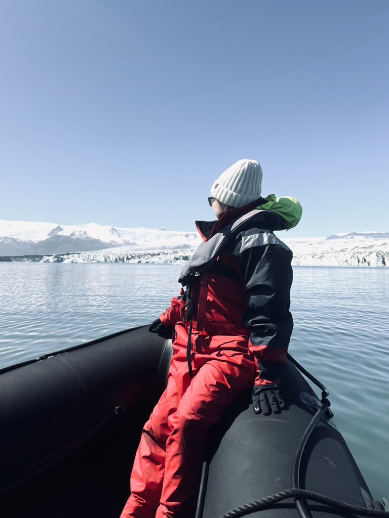 Girl in red immersion suit looking out at glacier while sitting on front of zodiac boat at Jökulsárlón Glacier Lagoon, Iceland