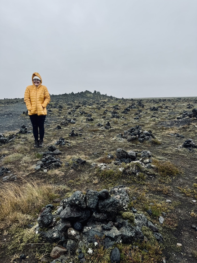 Girl in yellow coat standing in lava fields with rock piles in Iceland