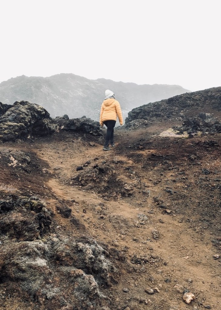 Girl in yellow coat walking through misty lava field around Mytavn, Iceland