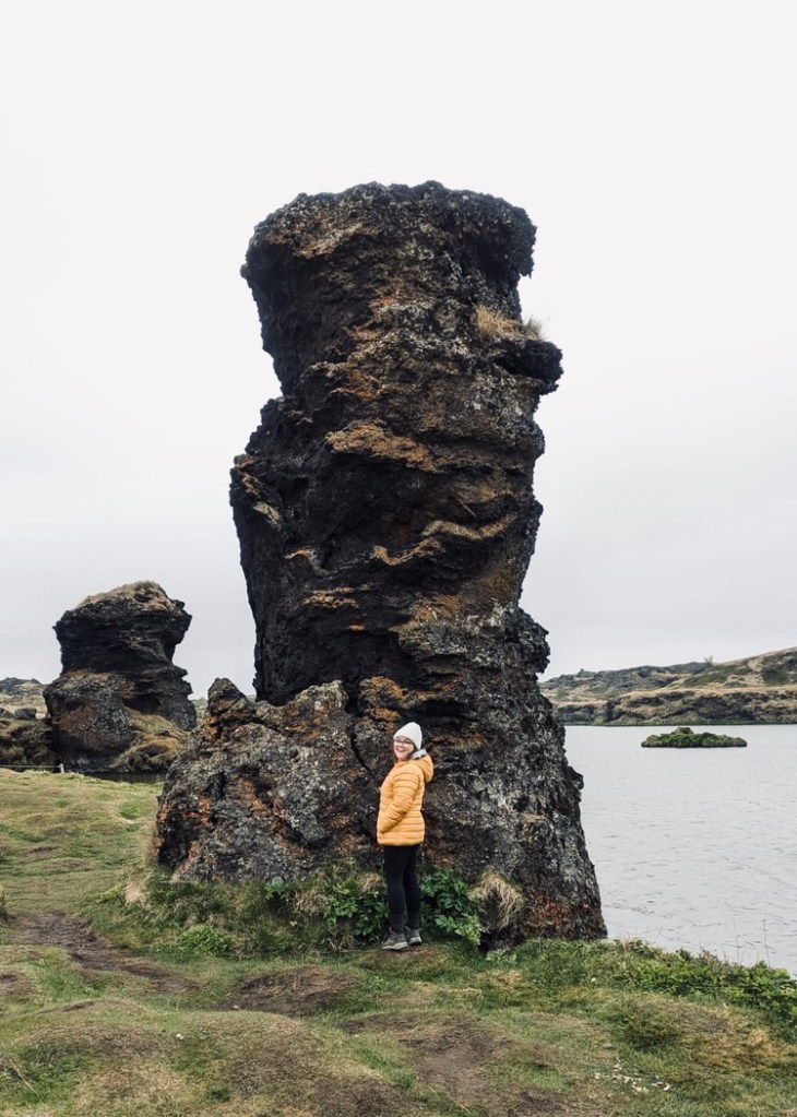 Girl in yellow coat standing next to lava rocks around Mytavn, Iceland