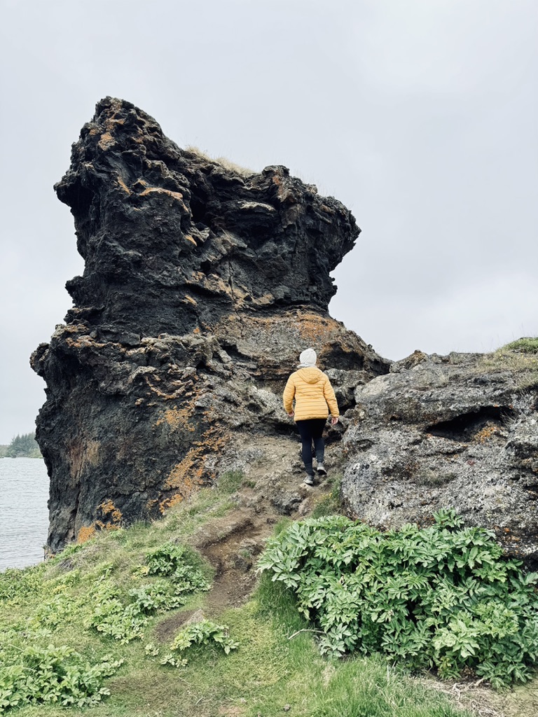 Girl in yellow coat climbing lava rocks around Mytavn, Iceland