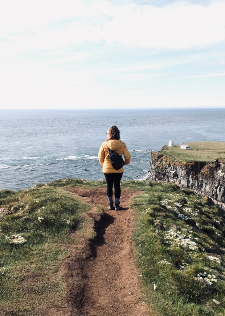 Girl in yellow coat looking out at view of ocean from Puffin Cliffs