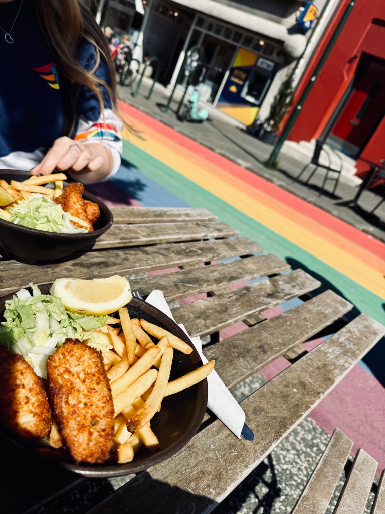 A bowl of fish and chips on a table with rainbow road in background in Reykjavik, Iceland