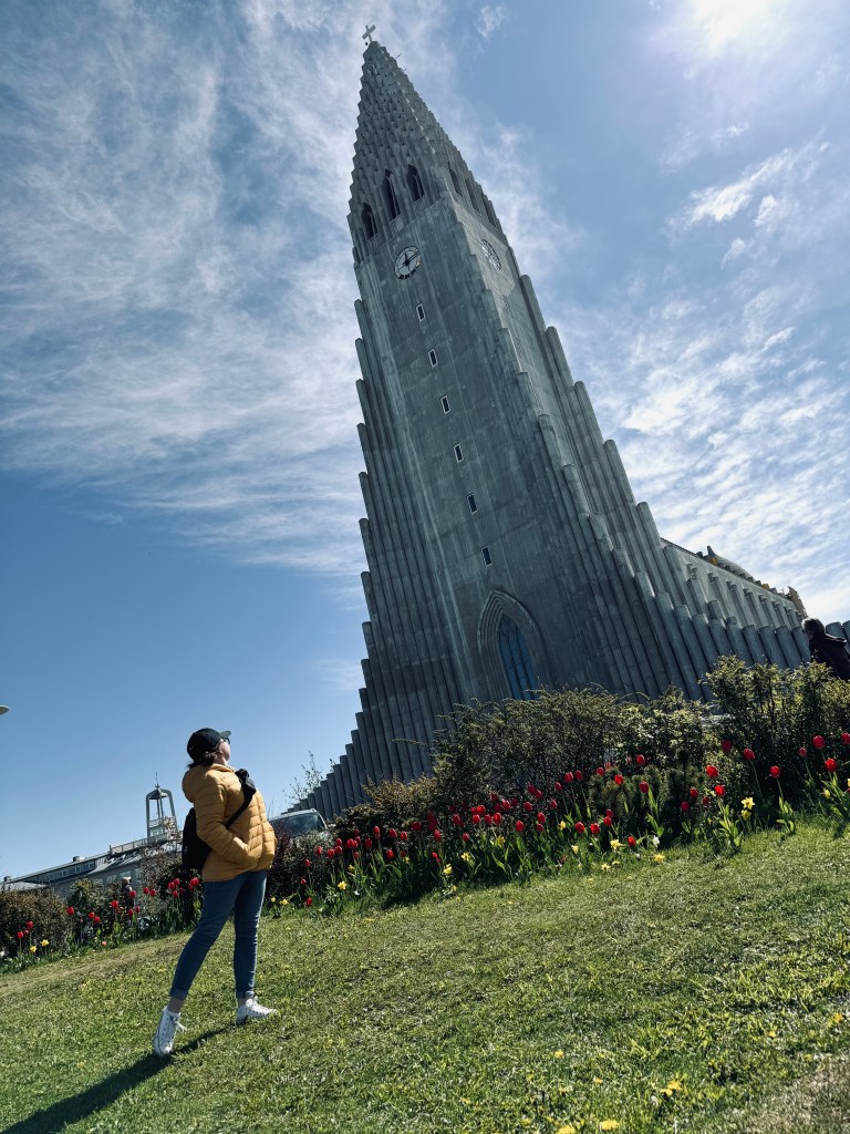 Girl in yellow coat looking up at Hallgrimskirkja church in Reykjavik, Iceland on a sunny day