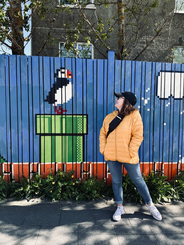 Girl in yellow coat smiling next to Mario-themed street art in Reykjavik Iceland
