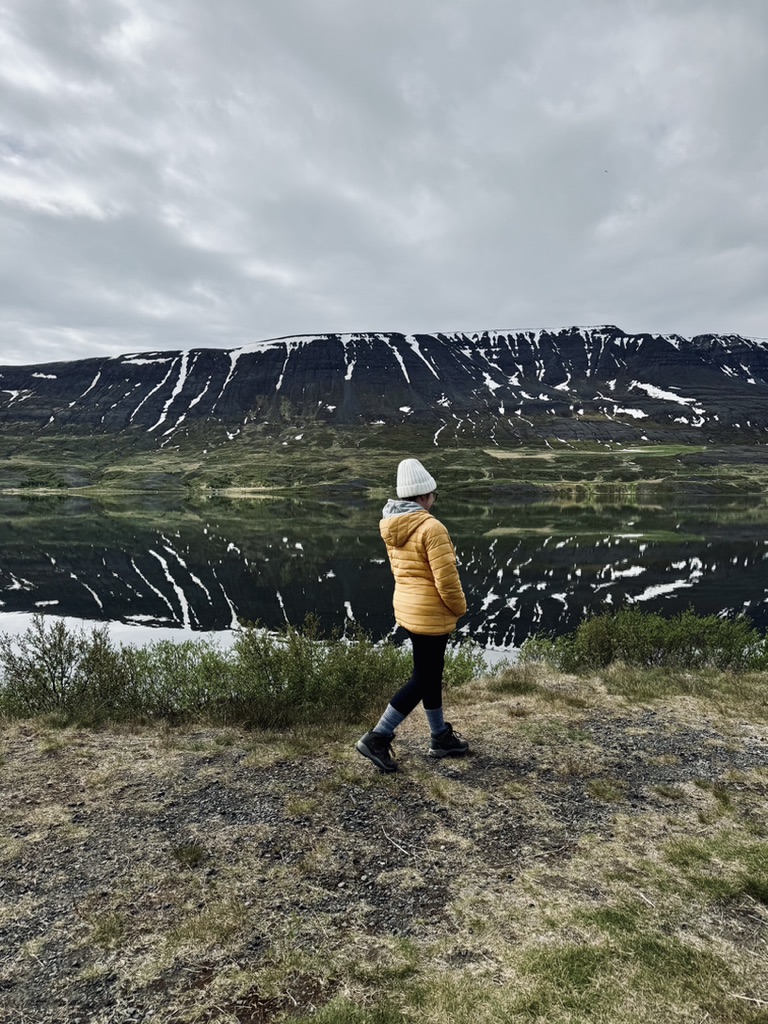 Girl in yellow coat walking toward reflection lake with mountains in Iceland