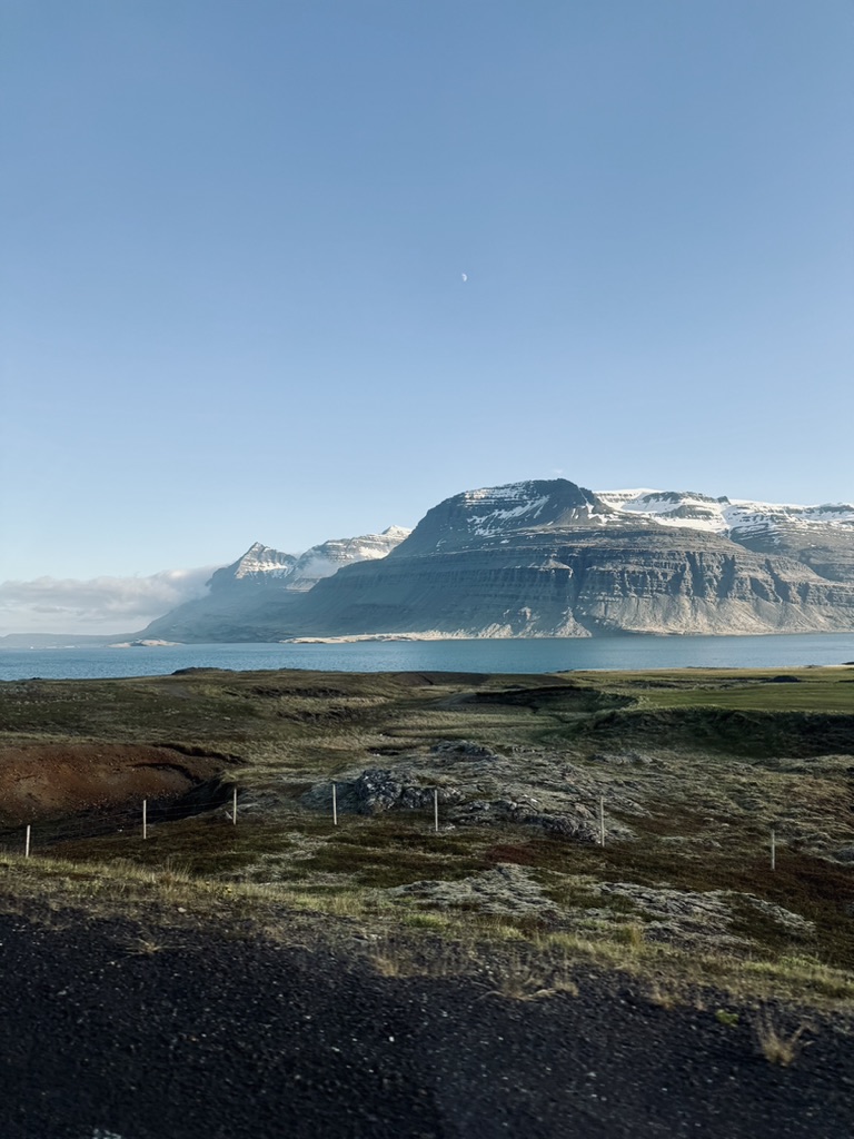 Dramatic rounded snow mountains with ocean and fields in East Fjords, Iceland