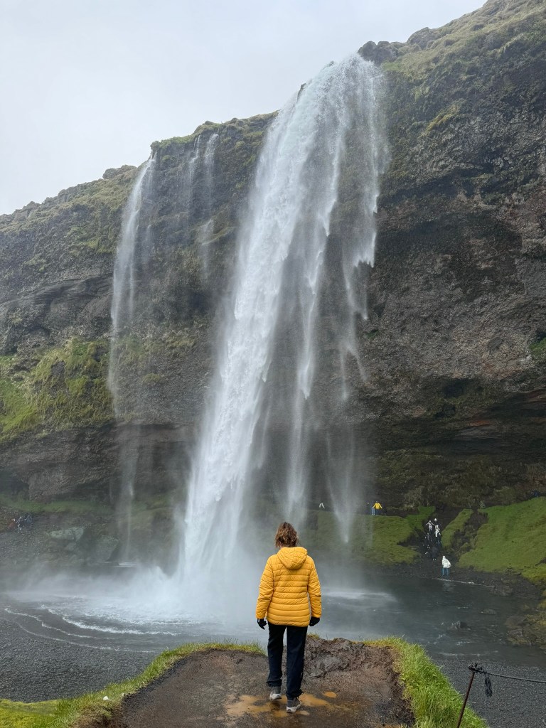 Girl in yellow coat looking out at Seljalandafoss waterfall, Iceland