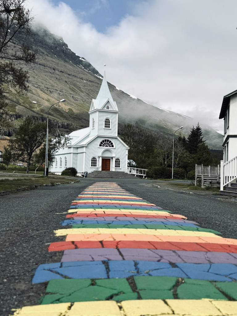 Famous little blue church Seyðisfjarðarkirkja with rainbow road in East Iceland